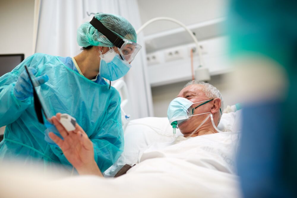 One nurse showing a framed photograph of a relative to a COVID patient.